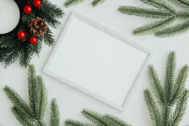 Boş bir kart merkezde duruyor, yemyeşil dallar ve kozalaklarla çevrili, sıcak ve davetkar bir atmosfer yaratıyor bayram kutlamaları için mükemmel..