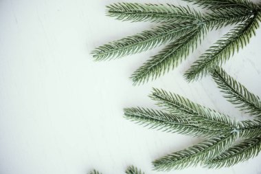 Freshly cut green pine branches lie gracefully on a light wooden surface, creating a natural and serene atmosphere perfect for seasonal decorations and crafts. clipart