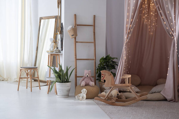 A welcoming playroom features a cozy nook draped in soft fabric, complete with plush toys, a wooden rocking horse, and decorative lights, creating a warm, inviting atmosphere for children.