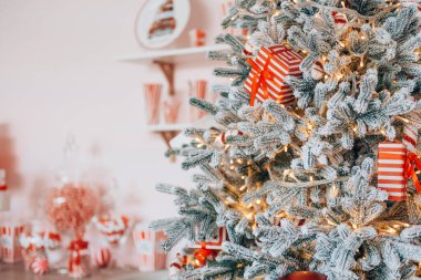 Noel ağacı kırmızı kurdeleler ve parıldayan ışıklarla süslenerek neşeli bir atmosfer yaratıyor. Yakınlarda, dekoratif eşyalar büyüleyici bir ortamda tatil ruhunu geliştirir..