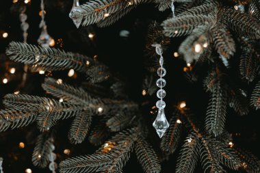 Delicate crystal ornaments dangle from the branches of a dark green Christmas tree, illuminated by warm white lights, creating a festive and inviting atmosphere during the holiday season. clipart