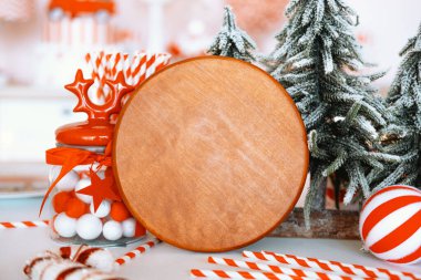 A rustic wooden plate sits on a table adorned with red and white decorations, including candy canes, ornaments, and frosted evergreen trees, creating a warm holiday atmosphere. clipart