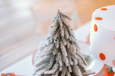 A decorative miniature Christmas tree is placed on a table, adorned with frosted branches. Nearby, a cake with red polka dots sits, creating a joyful holiday atmosphere. clipart