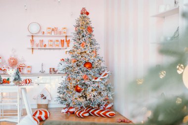 Güzel dekore edilmiş bir Noel ağacı, hoş bir odanın köşesini doldurur, kırmızı ve beyaz süslemelerle süslenir, şenlikli bir dekor ve neşeli bir atmosferle çevrelenir..