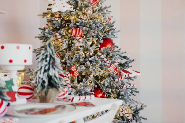 A beautifully adorned Christmas tree is displayed in a cozy room, featuring red decorations, candy canes, and twinkling lights, creating a warm holiday atmosphere. clipart