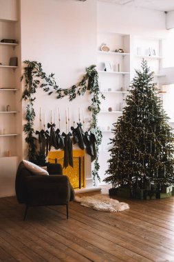 Tatil için dekore edilmiş sıcak ve davetkar bir oturma odasında güzel süslenmiş bir Noel ağacı ve asma çoraplı bir şömine bulunuyor..