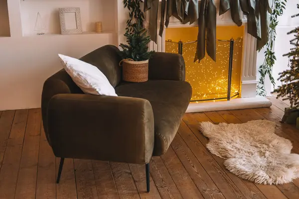 Oturma odasının şık bir köşesinde lüks bir kanepe, dekoratif yastık ve yeşil bitki bulunur. Parlak bir şömine ve tatil süslemeleri sıcak, davetkar bir atmosfer yaratır..