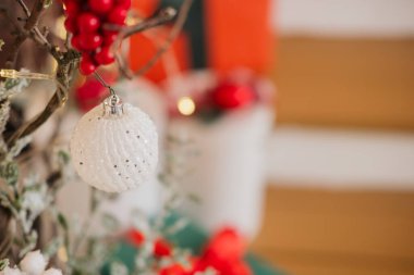 Güzel işlenmiş beyaz bir süs, parlak kırmızı böğürtlenlerle süslenmiş bir daldan sarkıyor. Çevreleyen odanın sıcak renkleri sıcak bir tatil atmosferi yaratır..