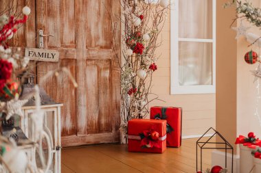 A cozy porch features a wooden door and festive red presents, accented by holiday decorations like branches and flowers. The space exudes warmth and holiday cheer, inviting guests in. clipart