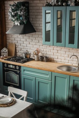 A cozy kitchen designed with mint green cabinets and a wooden countertop, adorned with holiday decorations. The space is well-lit, inviting, and functional for cooking and dining. clipart