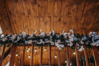 Süsler ve çiçeklerle süslenmiş güzel bir çelenk ahşap bir tavana asılır. Yumuşak ışıklandırmayla sıcak ve davetkar bir tatil atmosferi yaratır..