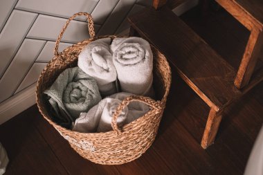 Temiz rulo havlularla dolu bir hasır sepet sıcak bir banyoda ahşap bir taburede oturur. Havlular kolay erişim için ayarlandı, dingin ortamı geliştirmek için..