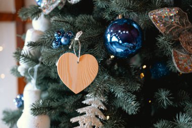 A beautifully decorated Christmas tree features vibrant blue and white ornaments, showcasing a simple wooden heart hanging among the festive decorations, creating a cozy atmosphere. clipart