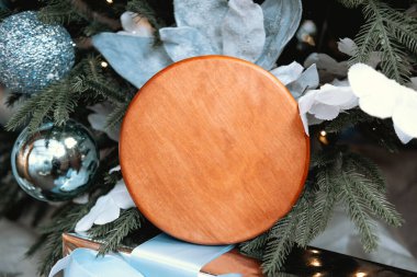 A round wooden board sits amidst shimmering blue and silver ornaments on a lovingly decorated holiday tree. It adds a rustic touch to the cheerful festive atmosphere. clipart