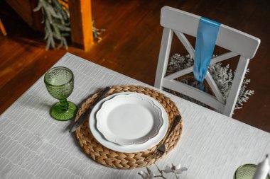 Güzel düzenlenmiş bir yemek masasında, üzerinde yeşil cam eşyalar ve şık çatal bıçaklar bulunan beyaz bir tabak, davetkar bir atmosfer yaratıyor..