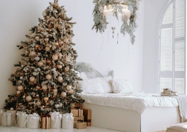 Güzel dekore edilmiş bir Noel ağacı, süslerle süslenmiş ve paketlenmiş hediyelerle çevrili ışık dolu bir odada duruyor. Sıcak atmosfer şenlik neşesini davet ediyor..