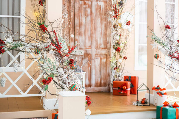 A cozy porch is adorned with festive decorations for the winter season, featuring vibrant ornaments, colorful presents, and seasonal greenery, creating a warm and inviting atmosphere.
