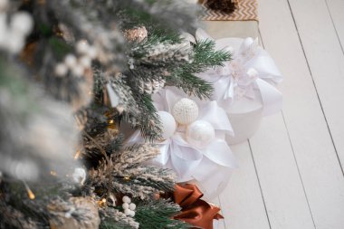 Dekoratif beyaz ve altın hediyeler şenlikli süslerle süslenmiş gür bir Noel ağacının altına yerleştirilir. Samimi ortam sıcak bir tatil ortamı yaratıyor..