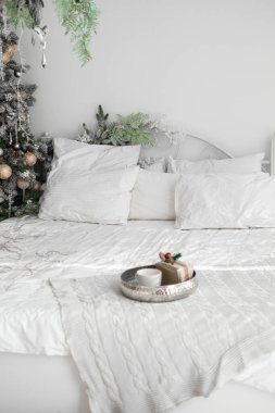 Davet edilen yatak odasında, yumuşak yastıklarla çevrili, beyaz çarşaflı, düzgünce yapılmış bir yatak var. Süslü bir Noel ağacı, sakin atmosfere şenlikli bir dokunuş ekler..