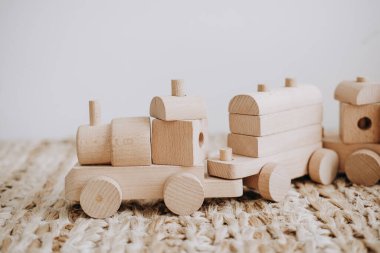 Yaratıcı oyun için dizayn edilmiş ahşap tren oyuncakları örülmüş bir hasırın üzerinde, doğal malzemelerin işçiliğini ve çocukluk yaratıcılığının neşesini vurguluyor..