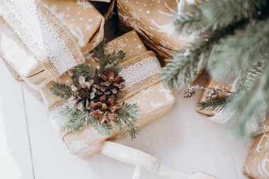 Kahverengi kağıda sarılmış, dantelli, kozalaklı ve yeşillikli hediyeler, sıcak ve davetkar bir atmosferde bir şenlik ağacının altında, büyüleyici bir tatil havası yaratıyor..