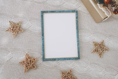 An empty picture frame sits on a knitted tablecloth, surrounded by golden star decorations. The setting has a warm, inviting feel, perfect for a holiday gathering or family memories. clipart