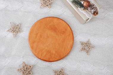 A round wooden serving board rests on a lace tablecloth, surrounded by decorative stars made of straw. Gifts wrapped with festive decorations are placed nearby, enhancing the holiday ambiance. clipart