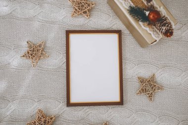 A blank decorative frame rests on a textured surface, surrounded by star-shaped ornaments and a beautifully wrapped gift box, creating a warm and inviting atmosphere. clipart