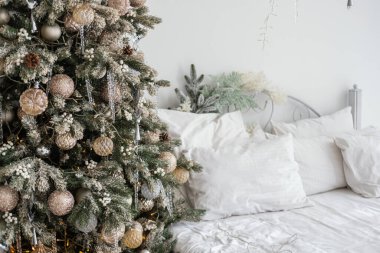 A warm, inviting bedroom features a decorated Christmas tree beside a neatly arranged bed. The soft bedding and festive ornaments create a cozy holiday atmosphere. clipart