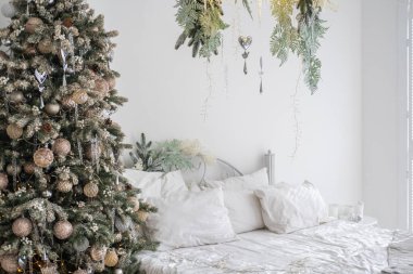 Konforlu bir yatak odasında altın ve gümüş süslerle süslenmiş bir Noel ağacı bulunuyor. Dekoratif yeşillik düzgünce yapılmış bir yatağın üzerinde asılı, sıcak bir tatil atmosferi yaratıyor..