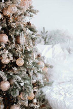 A festive Christmas tree adorned with shimmering ornaments and icicles stands in a cozy living room, evoking holiday warmth and joy, surrounded by soft white furnishings. clipart