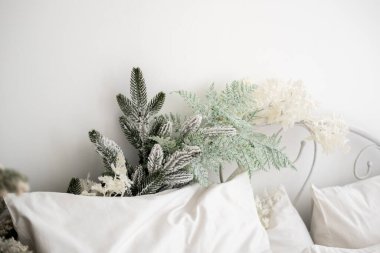 A cozy bedroom features a white bed adorned with fluffy pillows and frosted greenery resting at the headboard, creating a warm winter ambiance perfect for the season. clipart