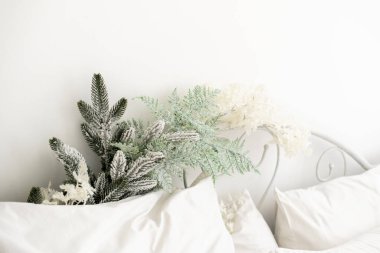 Rahat bir yatak odası yumuşak beyaz bir yatak odası sergiliyor yumuşak yastıklarla süslenmiş, buzlu yeşillikler ve narin çiçekler sergileniyor, serin bir kış atmosferi yaratıyor..