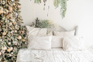 Huzurlu bir yatak odası, yumuşak beyaz çarşaflar ve yastıklarla düzgünce yapılmış bir yatağın yanında güzel süslenmiş bir Noel ağacını barındırır ve ılık bir tatil atmosferi yaratır..