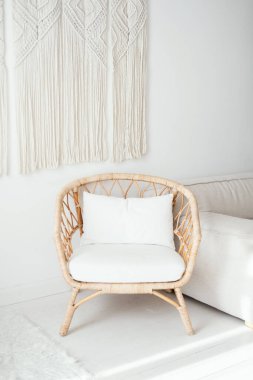 Yumuşak beyaz yastıklı bir rattan sandalye, doğal ışığın içeri aktığı minimalist bir oturma odasında davetkar bir şekilde oturur ve uzayın sıcak atmosferini arttırır..