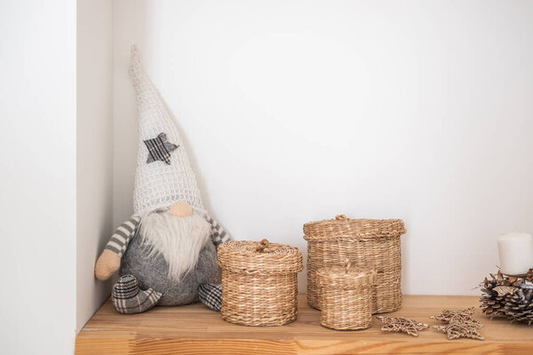 A whimsical gnome with a star hat sits beside three woven baskets on a light wooden shelf. The clean and minimalistic corner offers a warm and inviting atmosphere.