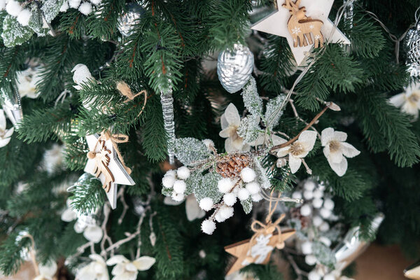 The Christmas tree is elegantly adorned with wooden ornaments, frosted flowers, and delicate garlands, creating a festive atmosphere perfect for the holiday season.