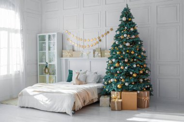 Güzel dekore edilmiş bir yatak odasında hediyelerle çevrili süs ve ışıklarla süslenmiş uzun bir Noel ağacı sergilenir. Yumuşak güneş ışığı boşluğu doldurur ve sıcak bir tatil atmosferi yaratır..