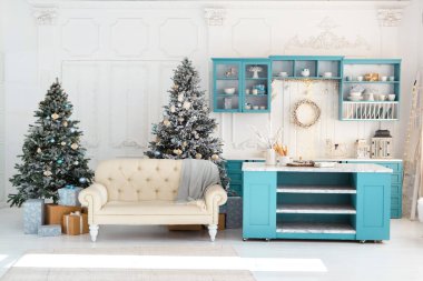 Oturma odasında krem renkli bir kanepe, iki dekore edilmiş Noel ağacı ve mevsimlik dekorlarla süslenmiş parlak mavi bir mutfak dolabı bulunuyor..