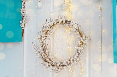 Dal ve pamuktan yapılmış dekoratif bir çelenk, yumuşak peri ışıklarıyla güçlendirilmiş bir duvarı süslüyor. Kış kutlamaları için mükemmel sıcak bir ortam yaratıyor..