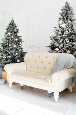 A charming living space features a cream tufted sofa draped with a soft throw, surrounded by two beautifully decorated Christmas trees adorned with ornaments and lights, creating a festive atmosphere. clipart