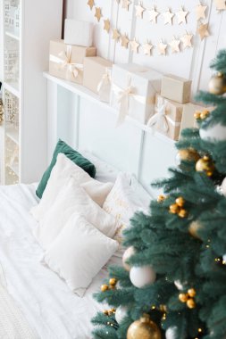Tatil için dekore edilmiş büyüleyici bir oturma odası, süslerle süslenmiş bereketli bir Noel ağacı ve beyaz bir kanepenin üzerinde güzelce paketlenmiş hediye kutuları..
