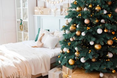 Konforlu bir yatak odasında, süslerle ve ışıklarla süslenmiş güzel dekore edilmiş bir Noel ağacı, sarılı hediyeler ve yatağın üzerine sıcak bir battaniye bulunur..