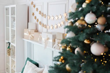 Şenlikli bir oturma odasında güzel dekore edilmiş süslerle süslenmiş bir Noel ağacının yanı sıra duvarda sarılı hediyeler ve çelenkler sergilenerek sıcak bir tatil ortamı yaratılıyor..