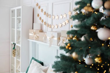 Konforlu bir oturma odasında güzel dekore edilmiş bir Noel ağacı parıldayan süsler ve altında güzelce paketlenmiş hediyeler bulunur. Altın yıldızlar duvarda asılı, sıcak bir tatil ortamı yaratıyor..