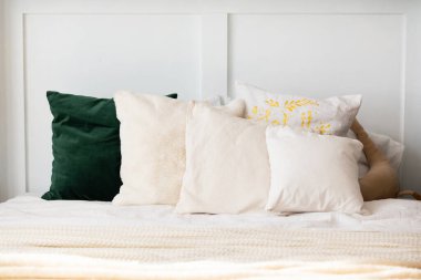 Farklı dokularda ve renklerde çeşitli dekoratif yastıklar düzgünce yapılmış bir yatakta düzenlenir. Yumuşak ışıklandırma sıcak ve davetkar bir atmosfer yaratır, sıcak hissi arttırır..