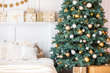 Konforlu bir yatak odasında altın ve beyaz süslemelerle bezenmiş bereketli bir Noel ağacı, güzelce paketlenmiş hediyelerle çevrili, sıcak bir tatil atmosferi yaratıyor..