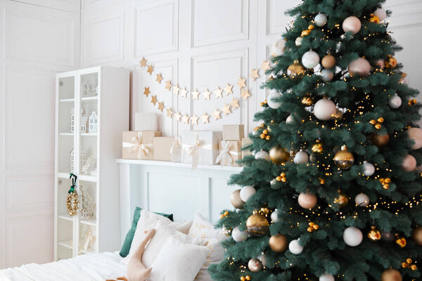 В этой уютной гостиной красиво украшена елка, украшенная золотыми и серебряными орнаментами. Подарки обернуты и помещены вокруг дерева, повышая праздничную атмосферу.