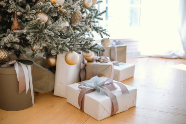 Güzel dekore edilmiş bir Noel ağacı, güzel paketlenmiş hediyelerle çevrili parlak bir oturma odasında duruyor ve uzaya sıcak ve şenlikli bir atmosfer ekliyor..