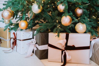 A collection of elegantly wrapped presents with bows sits under a festive Christmas tree adorned with golden ornaments and twinkling lights, creating a warm holiday atmosphere.